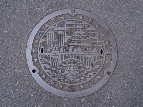 Osaka, Japan - November 20, 2015: A manhole cover in Osaka, Japan. A ship on Dotonbori canal and Osaka castle engraved on to a manhole cover as a symbol of an important city's landmark.