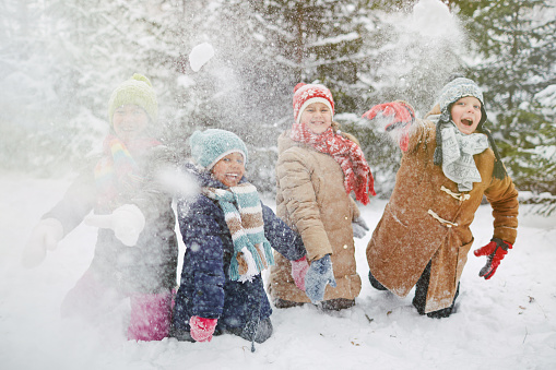 Happy children in winter-wear playing snowballs in park