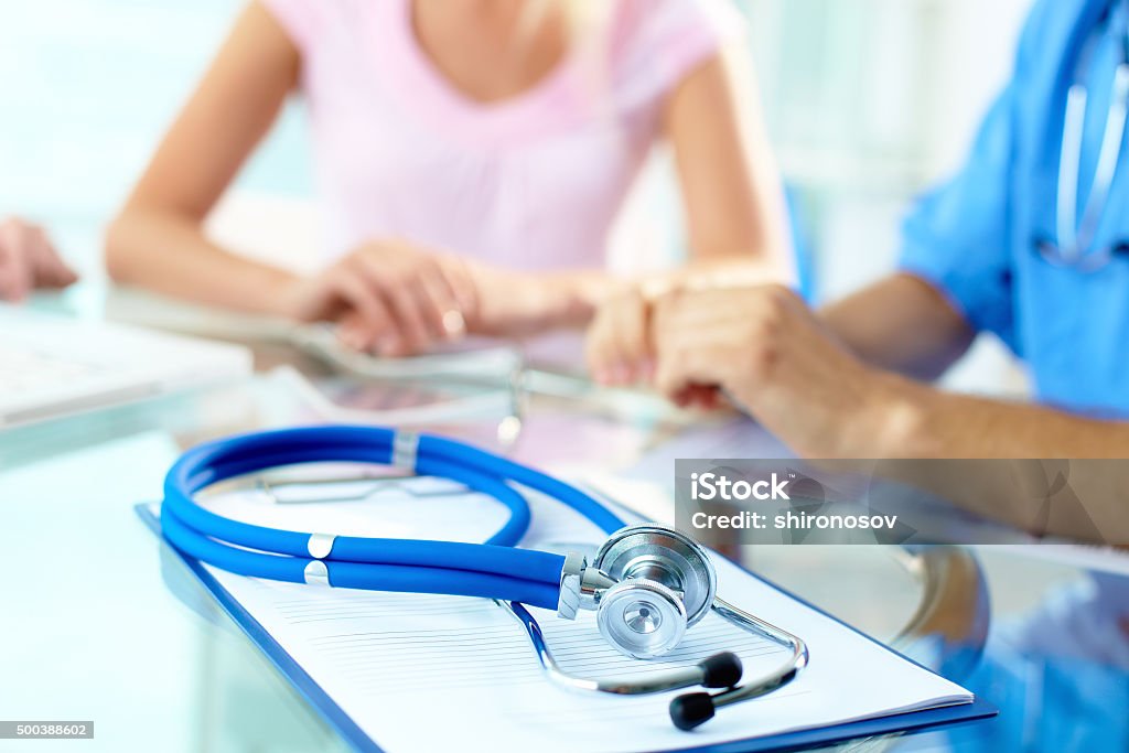 Stethoscope on clipboard Close-up of stethoscope and paper on background of doctor and patient hands Adult Stock Photo