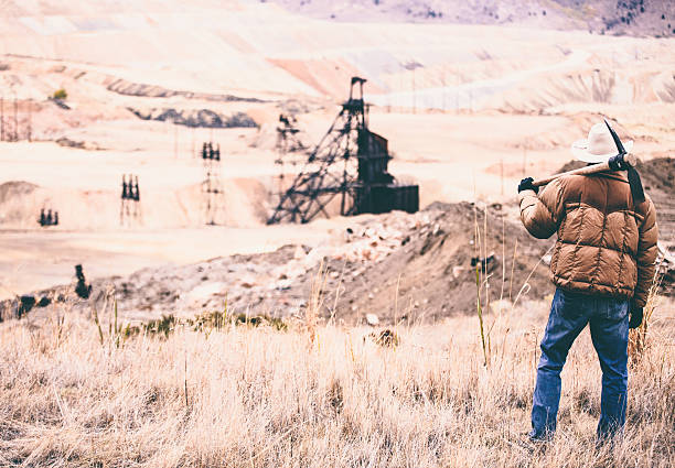 istock Rugged man looks at vast rock quarry with oil drill 500389697