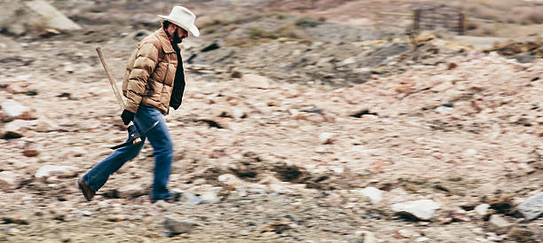 istock Rugged man walks across rocky field while carrying pickaxe 500389761