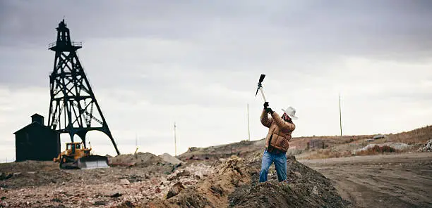 Photo of Cowboy swings pickaxe by old oil drill on western plain