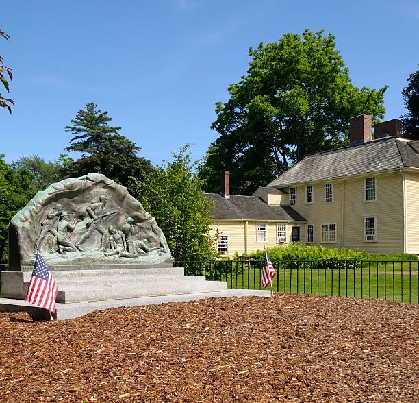 Lexington, Massachusetts, USA - June 10, 2012: The memorial dedicated to the Minute Men of the American Revolution in Lexington, Massachusetts. It was created by artist Basha Paeff in 1948. In the background stands Buckman Tavern, a place were members of the militia met at the dawn of the American Revolution.
