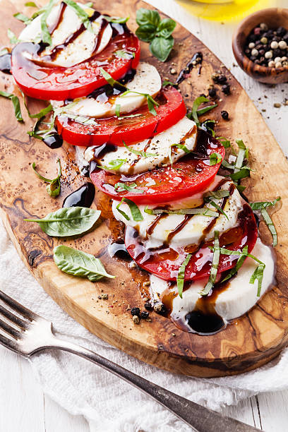 Caprese salad Caprese salad Tomato and mozzarella slices with basil leaves on olive wood cutting board balsamic vinegar stock pictures, royalty-free photos & images