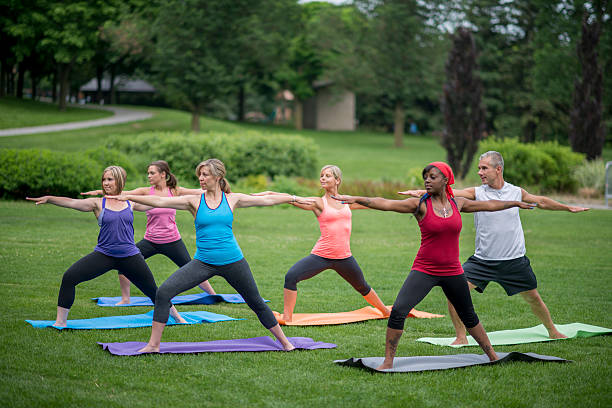 Reaching Forward in Warrior II Pose A multi-ethnic group of adults are standing in warrior two pose during their outdoor yoga class at the park. warrior 2 stock pictures, royalty-free photos & images