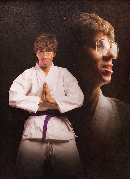 Karate Nerd Glamour Shot A nerdy looking young adult wearing a white gi and a purple belt poses for a martial arts themed portrait in a 1970's-1980's style studio glamour portrait.  Black background. nerd teenager stock pictures, royalty-free photos & images