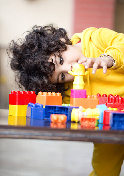 Little boy playing with colourful building blocks on table, Early Childhood Development. Children like to think hard about what they are doing and try out their own ideas. They can solve the problem of building blocks so they will stand high.