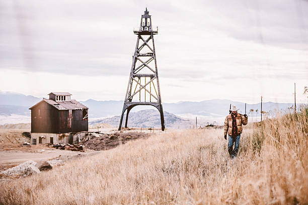 istock Man carrying pickaxe walking by old oil drill and barn 500403535