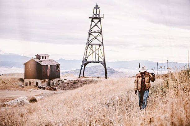 istock Man carrying pickaxe walking by old oil drill and barn 500403541