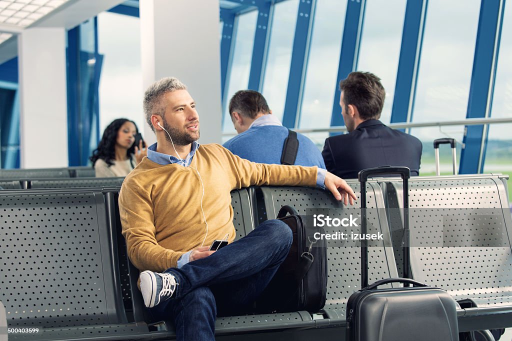 Waiting for the flight People waiting for a flight at the airport lounge. On the foreground an adult man wearing earphones and listening to the music. 30-34 Years Stock Photo