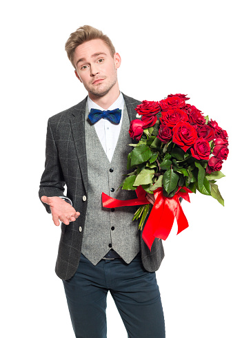 Portrait of disappointed elegant blonde young businessman holding a bunch of red roses. Studio shot, one person, isoleted on white. 