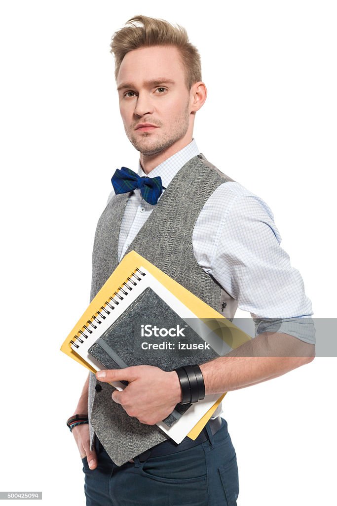 Fashionable man wearing tweed vest, holding notebooks Fashionable, confident young businessman wearing tweed vest and bow tie, holding notebooks in hands, looking at camera. Studio shot, white backgound. Graphic Designer Stock Photo