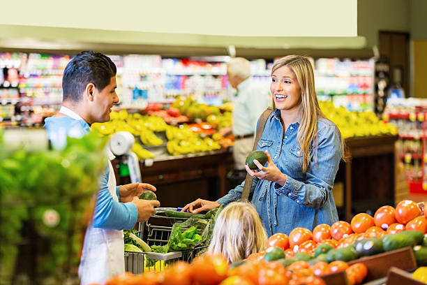 Customer selecting fresh produce while talking to supermarket employee