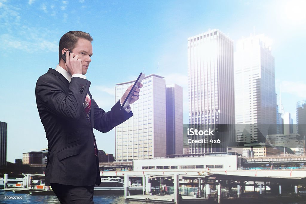 Businessman talking on mobile & using tablet Businessman talking on mobile & using tablethttp://www.twodozendesign.info/i/1.png Mobile Phone Stock Photo