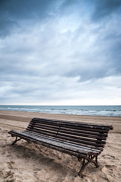 istock Old empty wooden bench stands on sandy beach 500428132