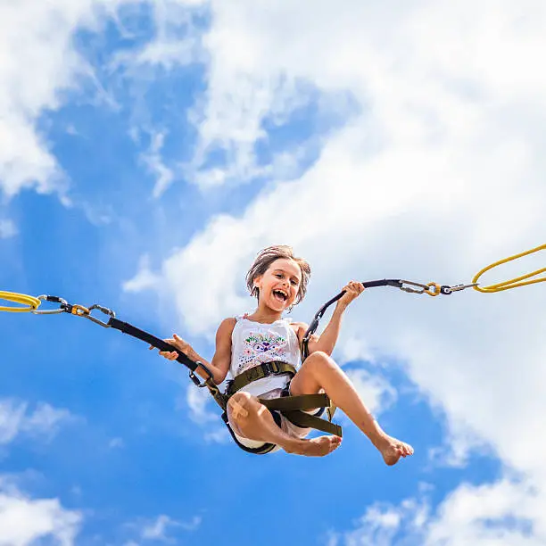 Little girl jumping at trampoline - flights against the blue sky 