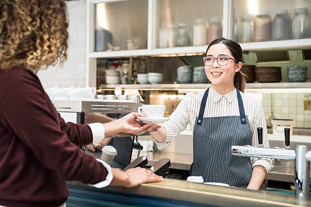 giovane asiatica barista che serve caffè femmina cliente in café - smiling women glasses assistance foto e immagini stock