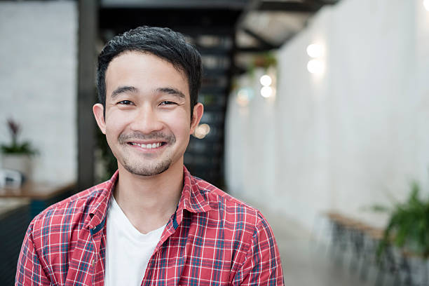 Casual young Asian businessman smiling towards camera, portrait Attractive male office worker wearing checked shirt looking at camera, smiling. Happiness, confidence, individuality, attractive male. 25 year old man portrait stock pictures, royalty-free photos & images