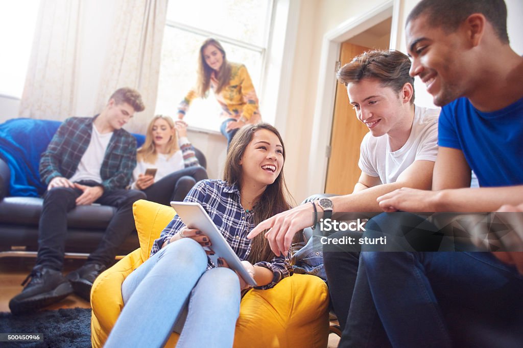 students sharing a house six young students sit around in their halls of residence , chatting and socialising with mobile phones and digital tablets. Three women and three men sit on sofas , beanbags and window ledges chatting and laughing . Teenager Stock Photo