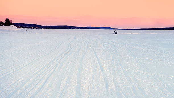 Snowmobile is driving on the frozen river at dusk.