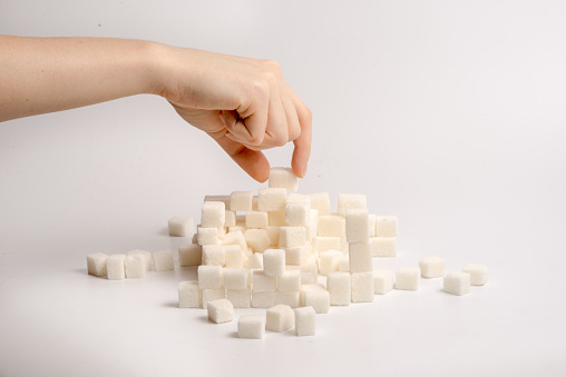 an arm building sugar cubes in a stack on white background