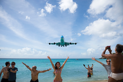 Maho Beach, St. Maarten - November 17, 2015: People at Maho Beach pose for pictures as a KLM Boeing 747 comes in for a landing at Princess Juliana International Airport in St. Maarten.