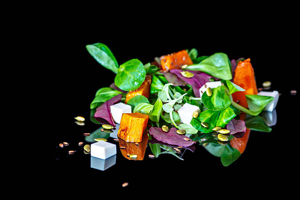 \nFresh vegetables salad with reflection on a black background, lettuce, pumpkin, sunflower seeds, feta.