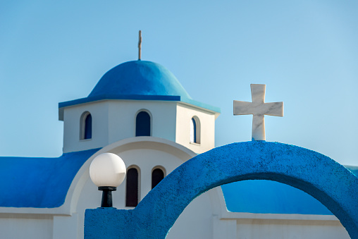 Entrance of A church with a blue dome and a white cross against a blue sky. Kos, Greece