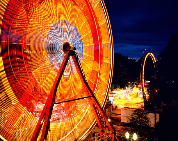longue exposition de grande roue à un carnaval - blurred motion amusement park spinning lighting equipment photos et images de collection
