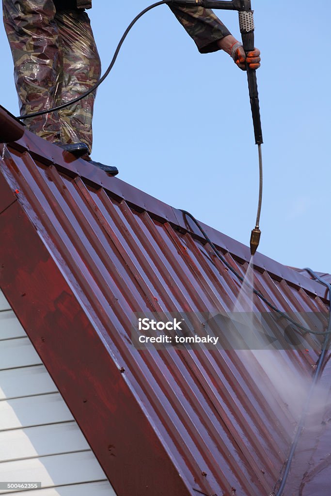 Professional roof washing. Worker on top of roof, with high pressure washer, cleans layer of old roof Rooftop Stock Photo