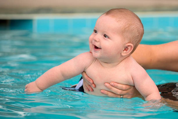 Happy infant baby boy enjoying his first swim in pool