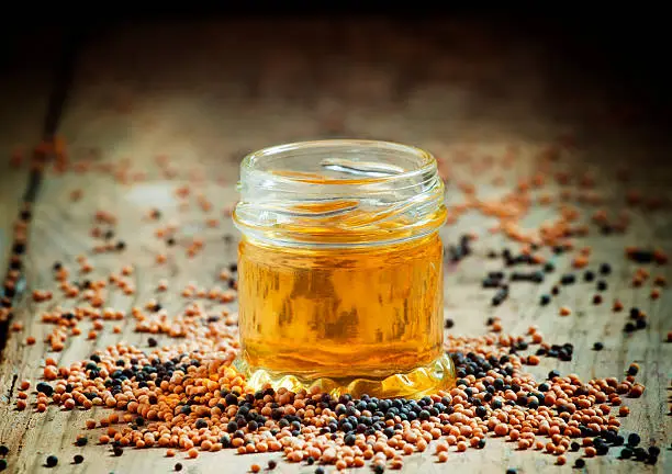 Oil of mustard in a small jar and yellow and black mustard seeds on an old wooden table in rustic style, selective focus