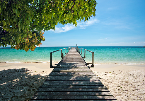 Wooden jetty in tropical beach of Ko Samet island, the shadow from the coastline tree is at foreground, Thailand