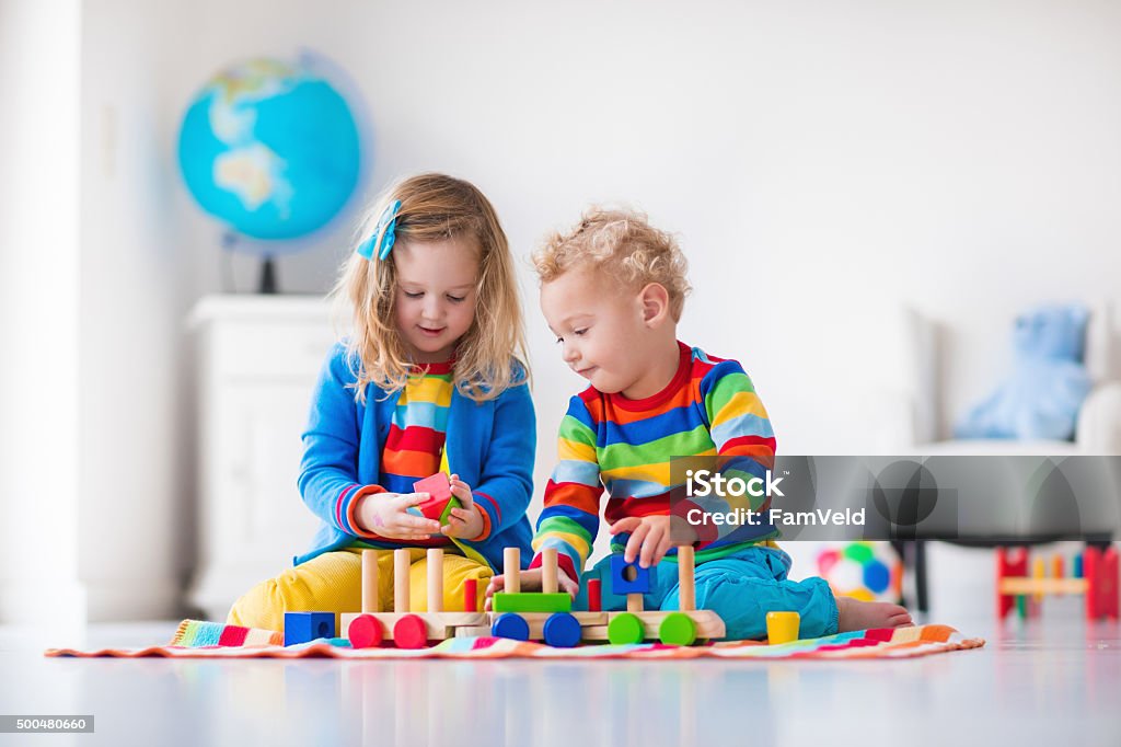 Kids playing with wooden toy train Children playing with wooden train. Toddler kid and baby play with blocks, trains and cars. Educational toys for preschool and kindergarten child. Boy and girl build toy railroad at home or daycare. Playing Stock Photo