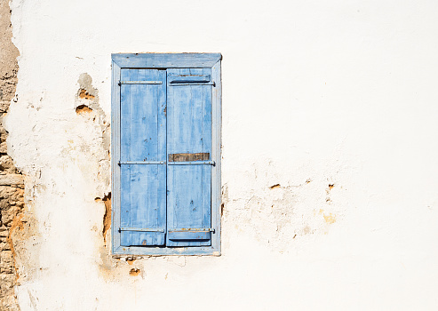 Mediterranean style old window. Blue on light wall with closed