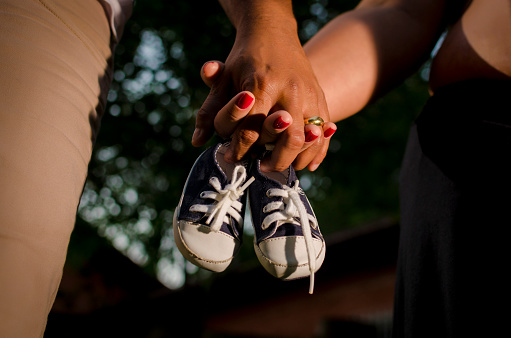Pregnant woman and her hasband holding hands, with baby's shoe whose they  are waiting for.