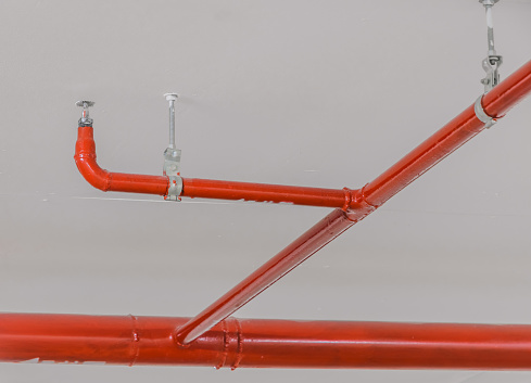 Fire sprinkler and red pipe on white ceiling background