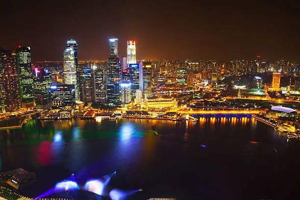 Aerial view of illuminated cityscape and skyline Singapore's. Above water of Bayfront is lasershow and some holograms are projected. In left half is financial district with bank towers and skyscrapers. In right half is river and Clarke Quay. Non editorial skyline shot with multiple logos and skylines, no logo in special focus, new guideline liscence.