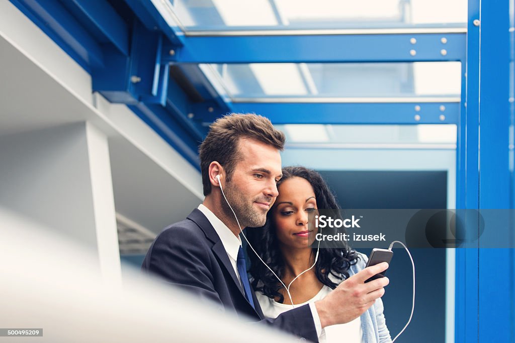 Listening to music together Business couple wearing earphone, listening to music together. Airport Stock Photo