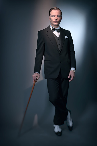Retro 1920 business fashion man wearing black suit and bow tie. Standing with cane. Studio shot.