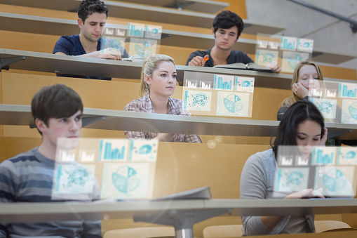 Focused students in lecture hall working on their futuristic tablet during lesson