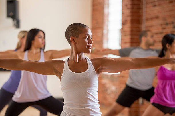 Focused in Warrior II Pose A multi-ethnic group of young adults are standing in warrior two pose during their yoga flow. spandex stock pictures, royalty-free photos & images