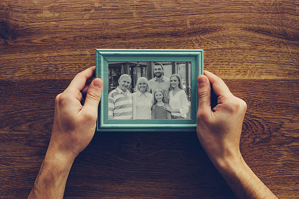 Close-up top view of man holding photograph of his family over wooden desk