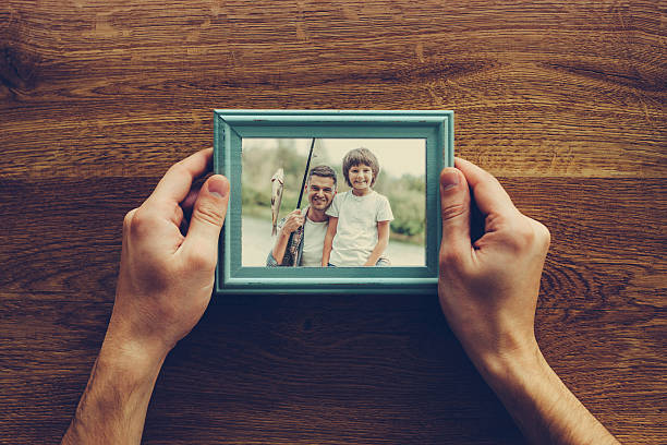 My son is my life. Close-up top view of man holding photograph of himself and his son fishing over wooden desk son photos stock pictures, royalty-free photos & images