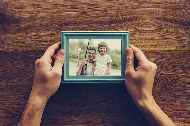 My son is my life. Close-up top view of man holding photograph of himself and his son fishing over wooden desk family pictures stock pictures, royalty-free photos & images