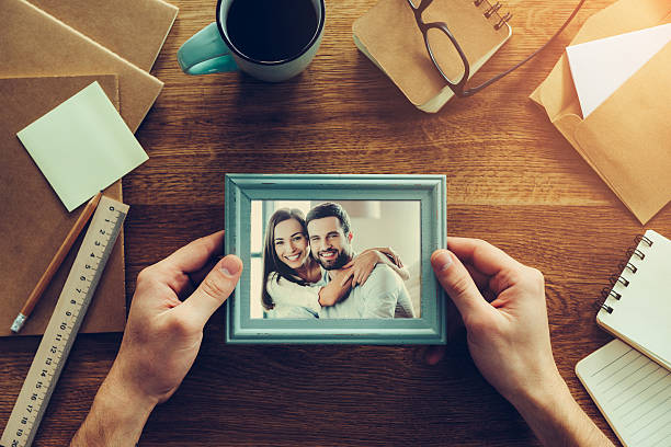 Bright moments together. Close-up top view of man holding photograph of young couple over wooden desk with different chancellery stuff laying around reminder photos stock pictures, royalty-free photos & images