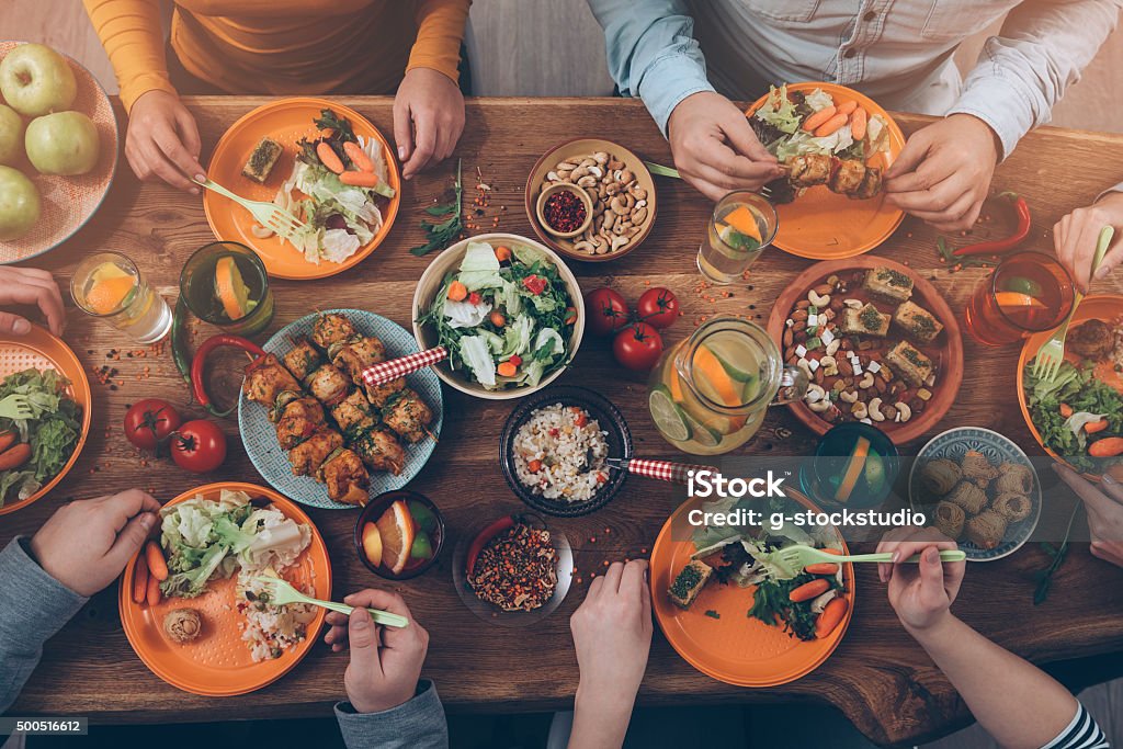 Enjoying dinner with friends. Top view of group of people having dinner together while sitting at the rustic wooden table Dining Table Stock Photo