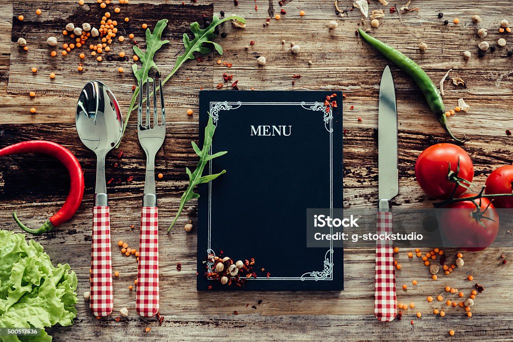 Restaurant menu. Top view of chalkboard menu laying on the rustic wooden desk with vegetables around Chalkboard - Visual Aid Stock Photo