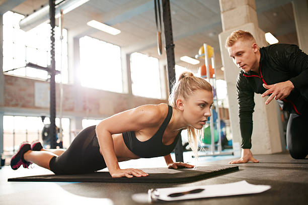 weibliche training mit einem persönlichen trainer im fitnessraum - athlete push ups muscular build female stock-fotos und bilder