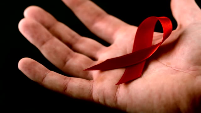 Aids red ribbon symbol falling over a man hand